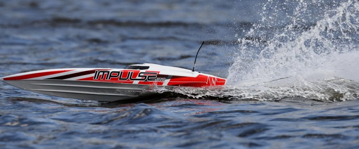 Picture of a red and white remote control boat racing on a lake