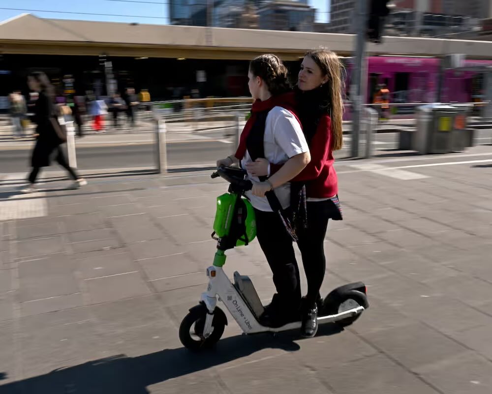 Image of two girls riding an electric scooter dangerously in a public area